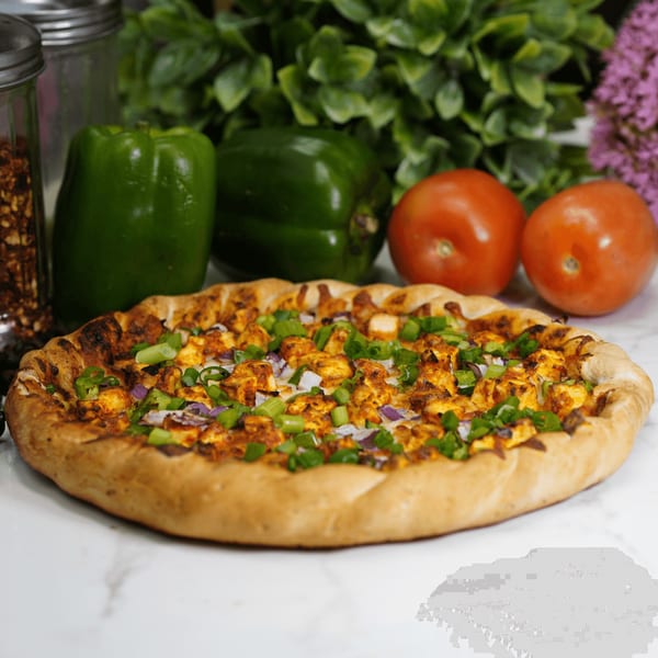 A chicken tikka pizza with green onions and red onions, surrounded by fresh vegetables.