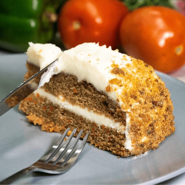 A slice of carrot cake with cream cheese frosting and a fork on a gray plate.
