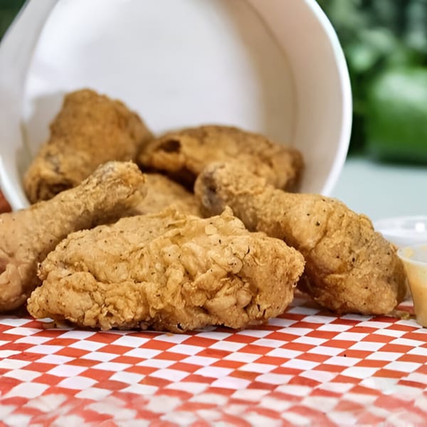 Crispy fried chicken pieces from Slice Pizza & Krunchy Chicken, spilling from a white bucket onto red checkered paper.