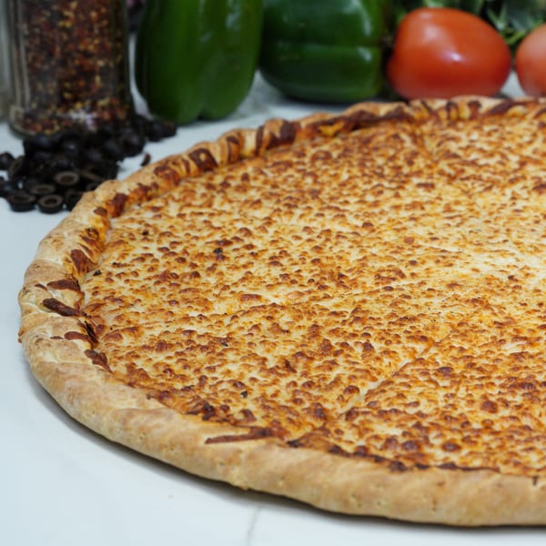A large, golden-brown cheese pizza with a thick crust, surrounded by fresh vegetables and spices.