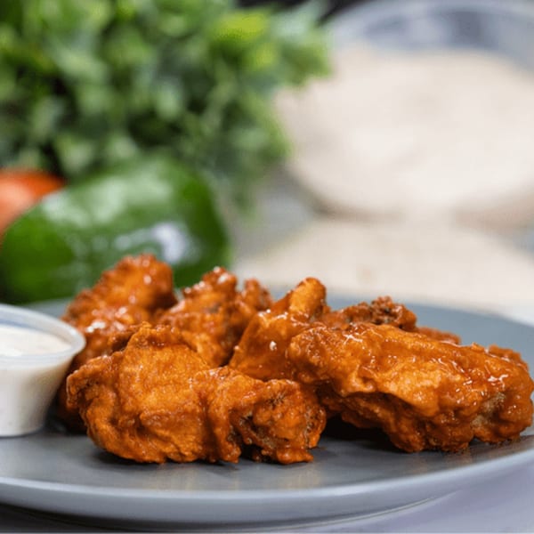 Plate of crispy, orange-glazed chicken wings with a side of ranch dressing and fresh vegetables.