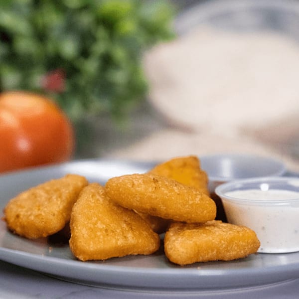 Golden-brown fried cheese curds on a gray plate with two dipping sauces and a tomato.