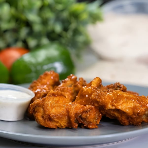 Plate of buffalo chicken wings with a side of ranch dressing, fresh vegetables in the background.