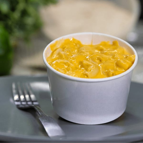 Creamy mac and cheese in a white cup, with a fork on a gray plate.
